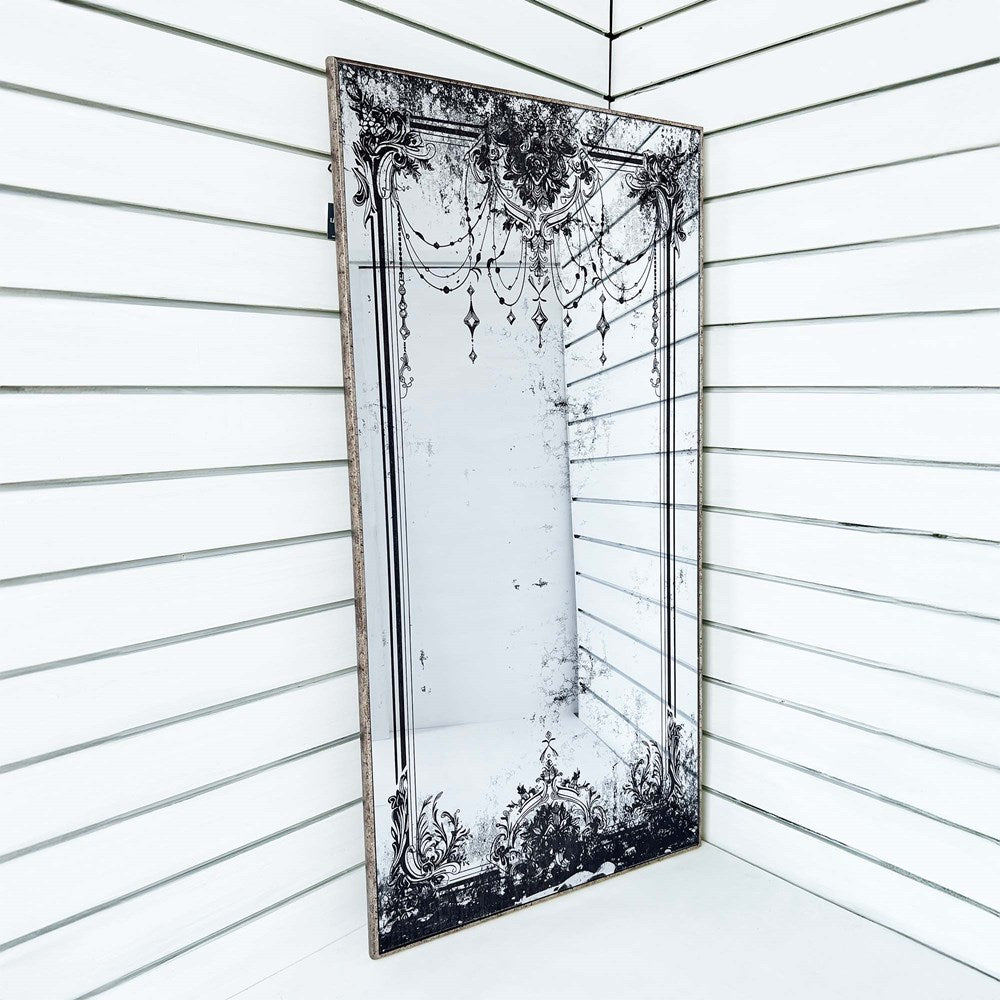 Decorative mirror with intricate black  design leaning against a white wall.
