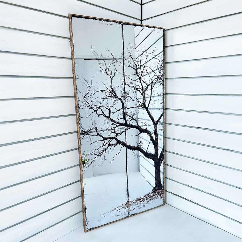 Decorative mirror with a tree on a white wall.