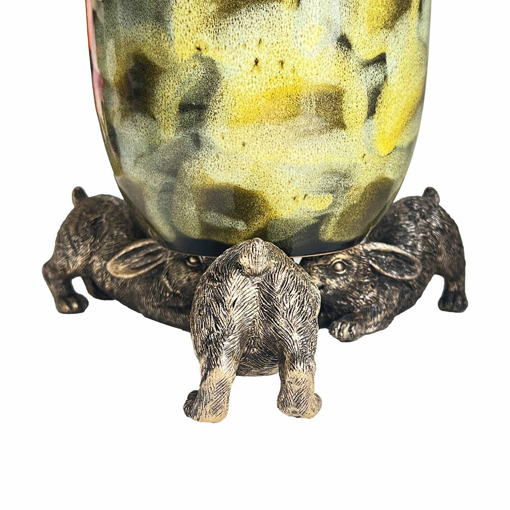 Decorative green multicolored pot balancing on the heads of three gold rabbits