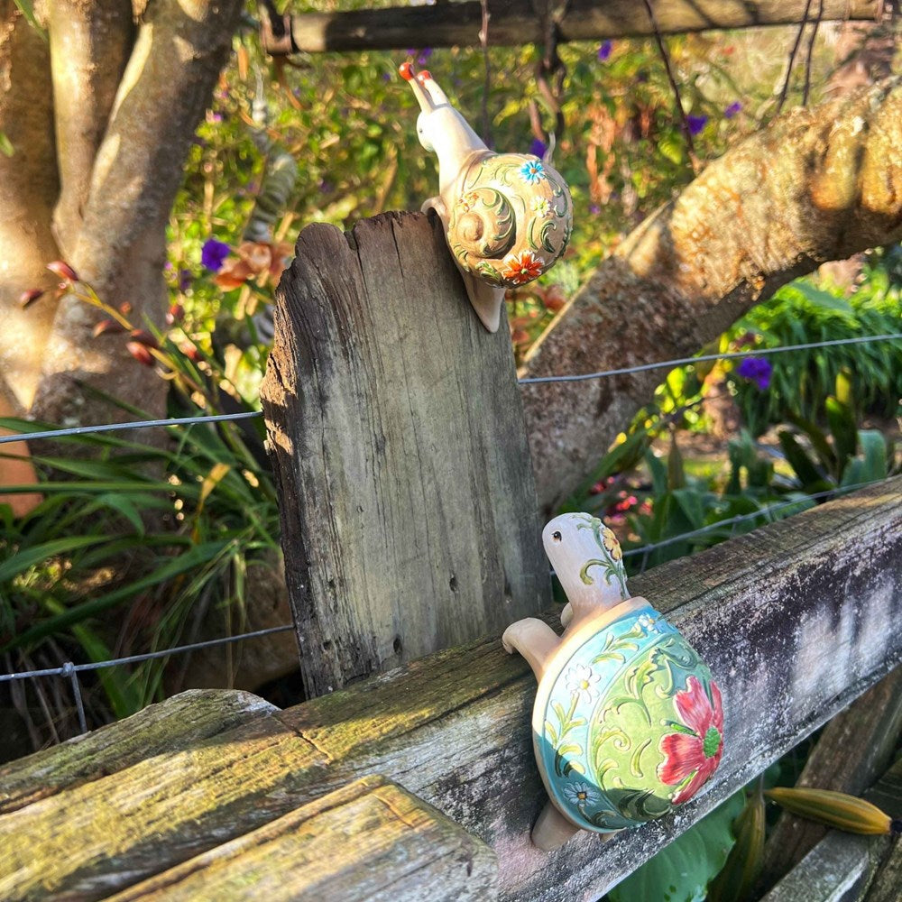 Decorative tortoise and snail figurines on a wooden fence with a garden background