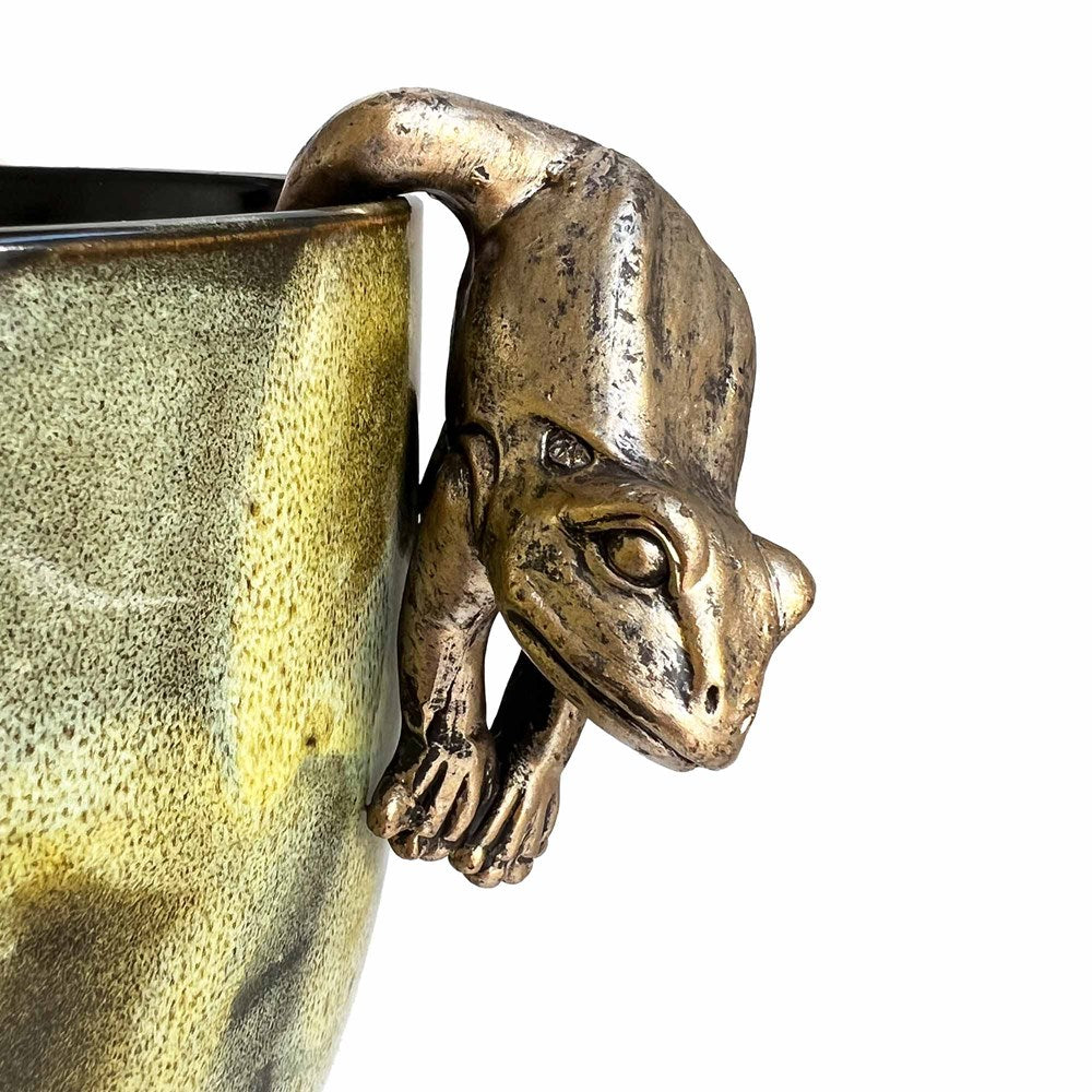 Gold frog hanging off a planter with a white background