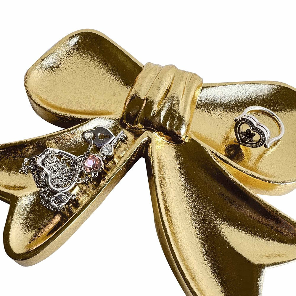 Gold bow shaped dish with jewellery displayed on a white background