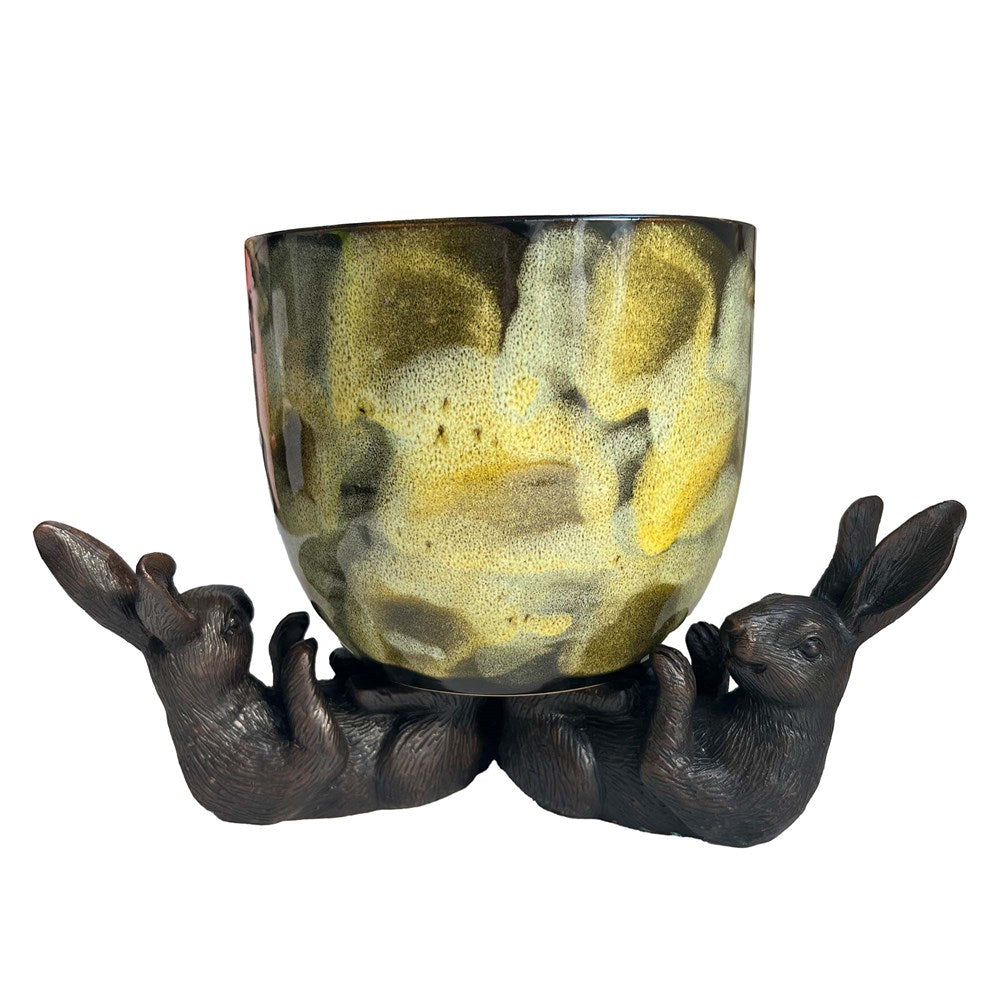 Hares holding with their feet a green patterned pot on a white background