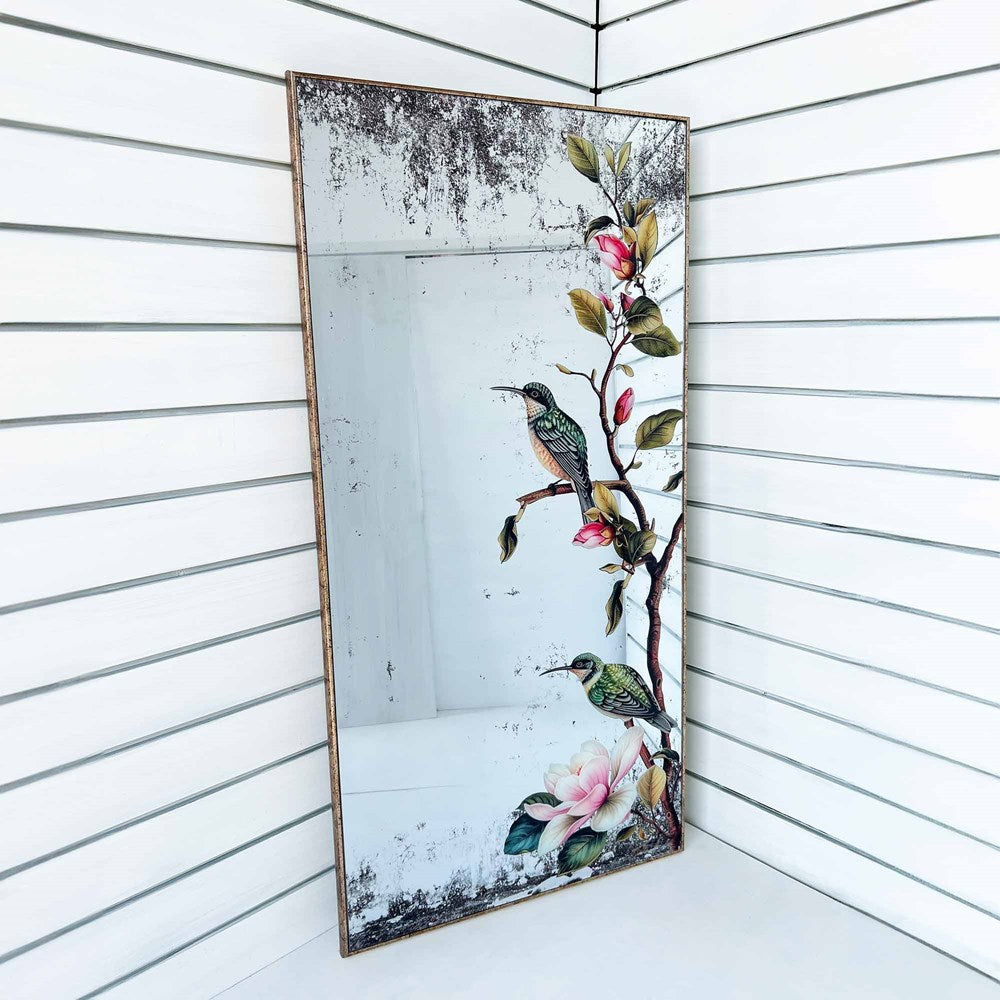 Decorative mirror with humming bird and floral design on a white wall.