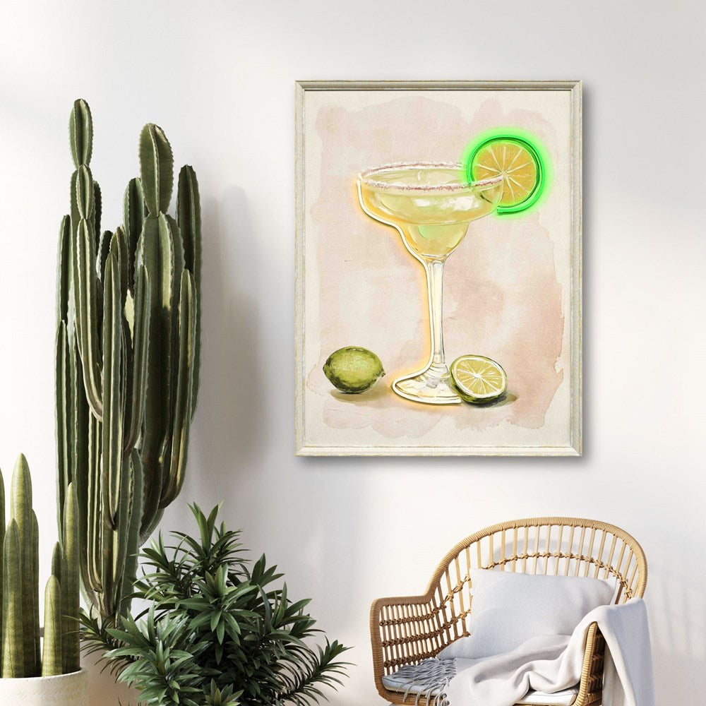 Framed artwork of a cocktail with lime slices on a wall above a wicker chair.