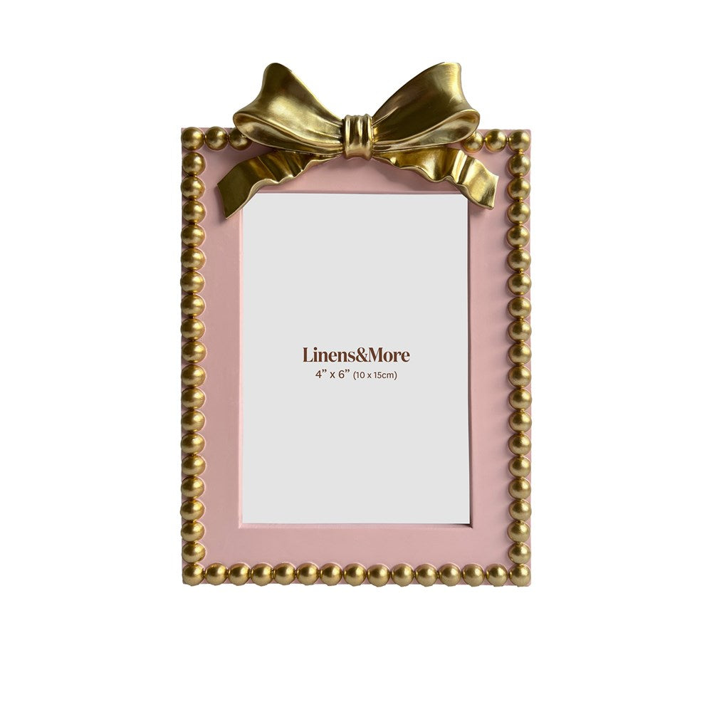 Pink picture frame with gold bow and 'Linens & More' branding on a white background