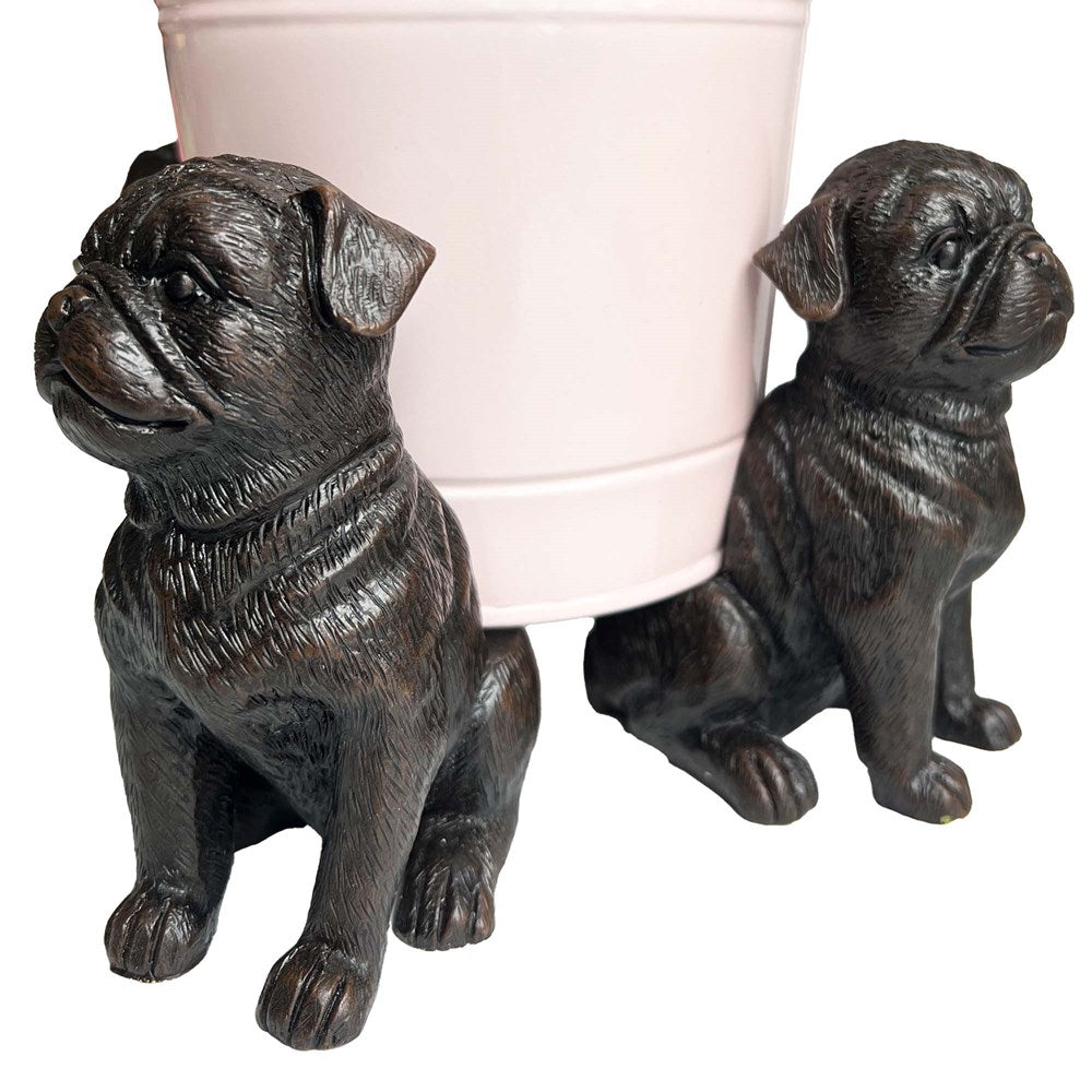 Two pug dogs statues holding a pink flower pot.