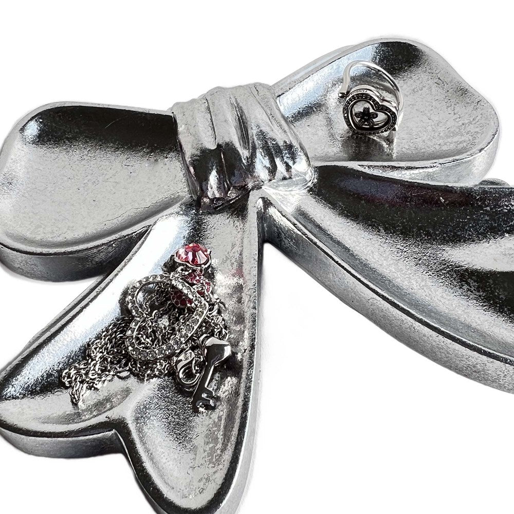 Silver bow shaped dish with a heart and chain jewellery on a white background