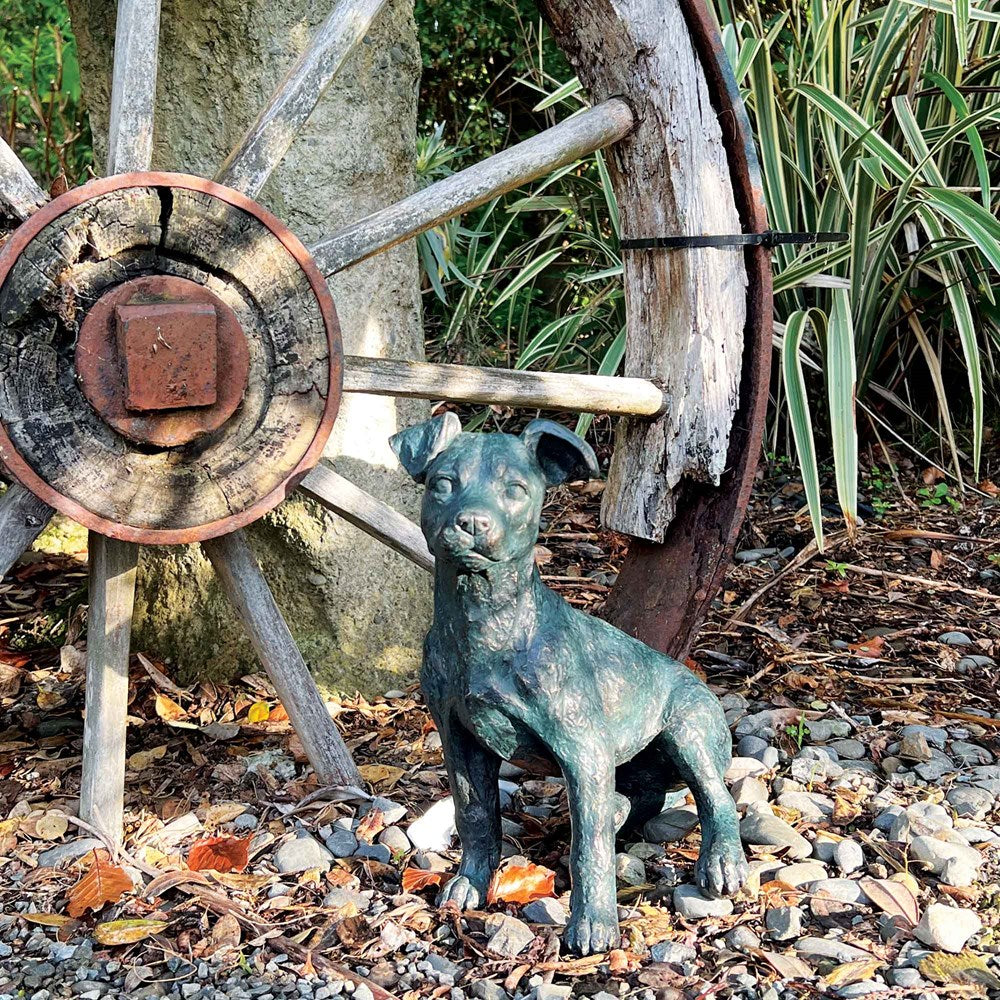 Dog statue in front of a rustic wooden wheel with a stone background