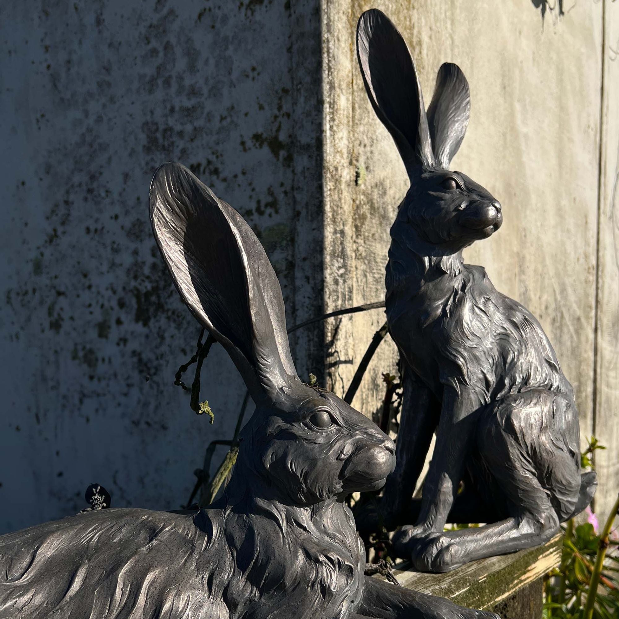 Two grey hares statues against a textured wall.