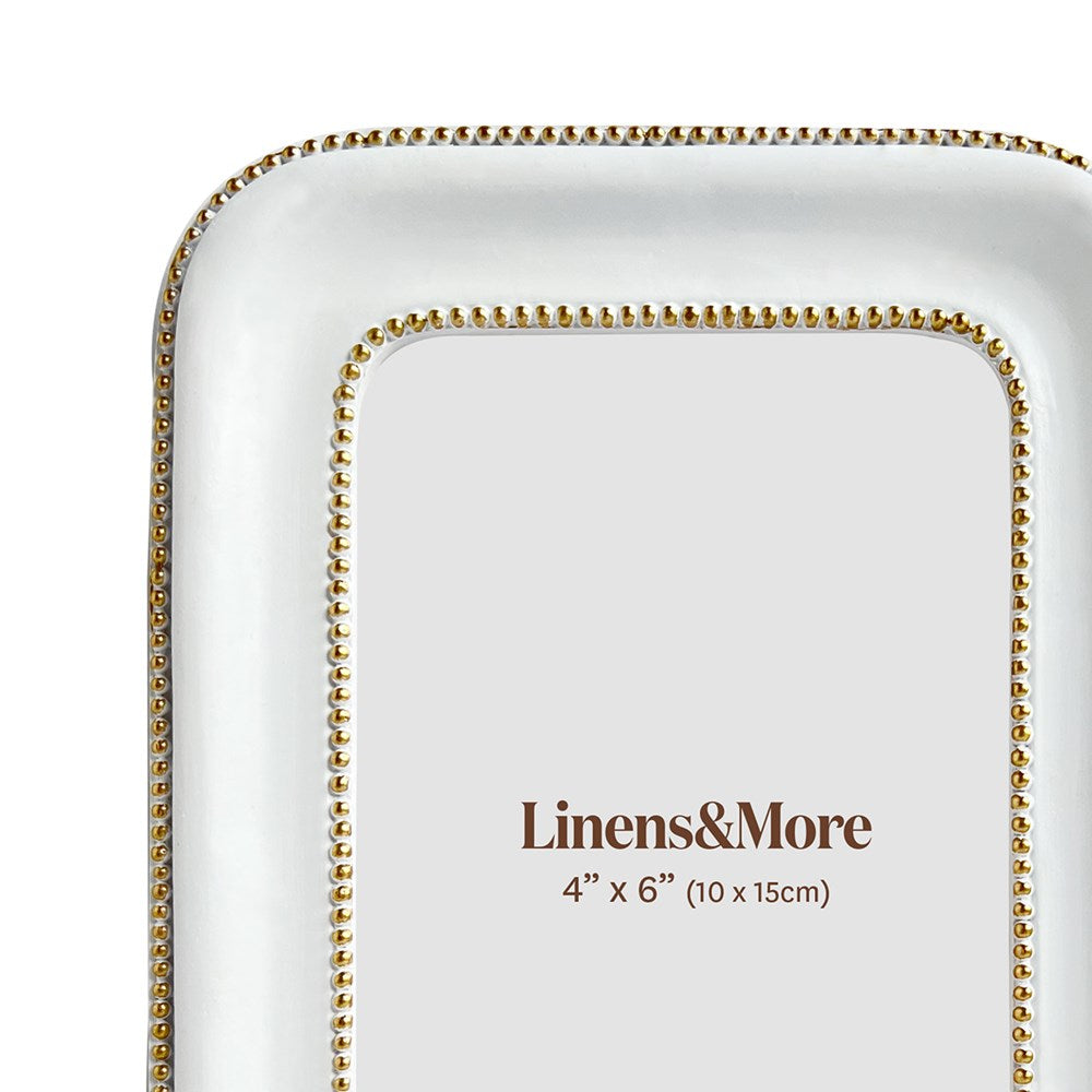White picture frame with gold beaded border and 'Linens & More' branding
